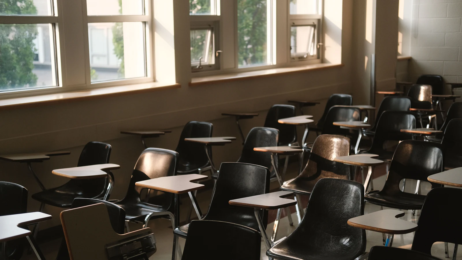 Salón de clases vacío con pupitres iluminados por la luz de la ventana.
