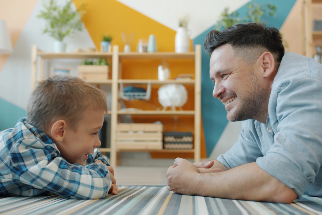 Un padre y su hijo conversan recostados en el suelo de la sala.